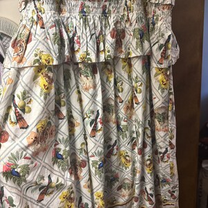 May include: A white dress with a floral and bird print. The dress has a tiered design with ruffled details and elasticated sections. The pattern includes tigers, birds, and flowers in various colours, set against a diamond grid.