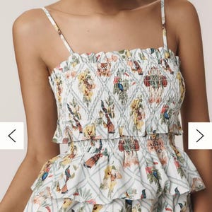 May include: A white dress with a colourful floral and bird print. The dress has a smocked bodice and tiered ruffles. The straps are thin, creating a feminine and summery style.