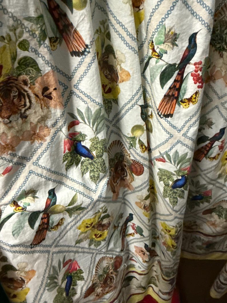 May include: White fabric featuring a repeating pattern of tigers, birds, butterflies, and flowers. The design includes a diamond grid with a chain-like border. The colour palette features shades of beige, green, yellow, and orange, creating a vibrant and detailed textile.