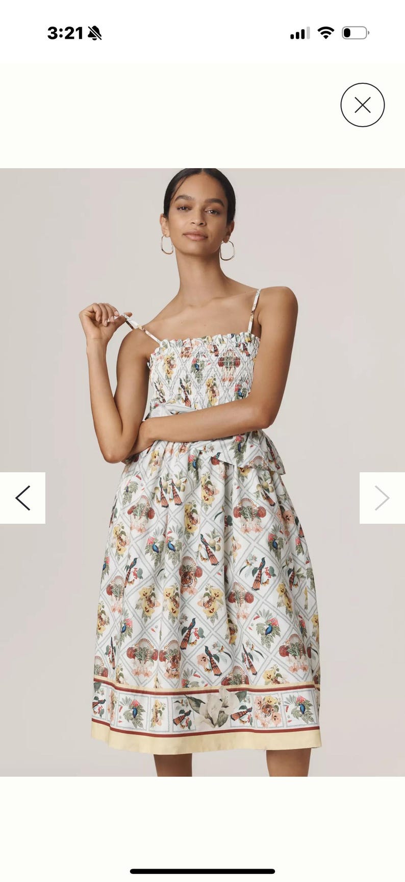 May include: A white sundress with a floral pattern featuring birds and flowers. The dress has a smocked bodice and spaghetti straps. The skirt is knee-length with a yellow hem.