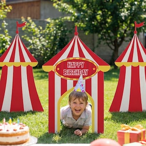 Può includere: Una scena di compleanno all'aperto con ritagli di tenda da circo a strisce rosse e bianche, palloncini, regali e una torta. Un bambino con un cappello da festa è all'interno di una delle tende. Il cartello sulla tenda dice "Happy Birthday".