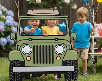May include: A green cardboard Jeep photo prop with children inside, surrounded by colorful balloons and a party setting. The Jeep has black tires, headlights, and a front grill. Children are smiling and holding a star-shaped balloon.