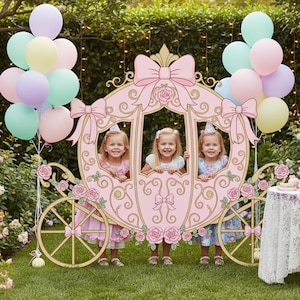 May include: A pink princess carriage photo prop with three children inside, surrounded by pastel balloons. A table with cupcakes and a lace tablecloth is set up nearby. The scene is outdoors in a garden setting.