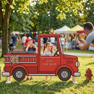 Könnte beinhalten: Ein roter Pappaufsteller eines Feuerwehrautos mit dem Text "CITY FIRE DEPT." Zwei Kinder sitzen im Fahrzeug, und ein Mann macht ein Foto. Vor dem Truck steht ein kleiner Tisch mit Megaphon und Feuerlöscher.