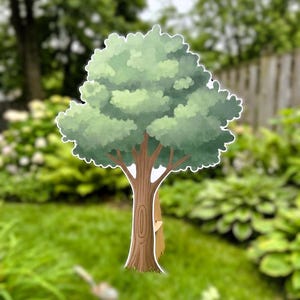 May include: A whimsical tree-shaped yard decoration with a light brown trunk, green leaves, and a white outline. The tree has a small animal peeking out from behind it. The background is a blurred green lawn and foliage.