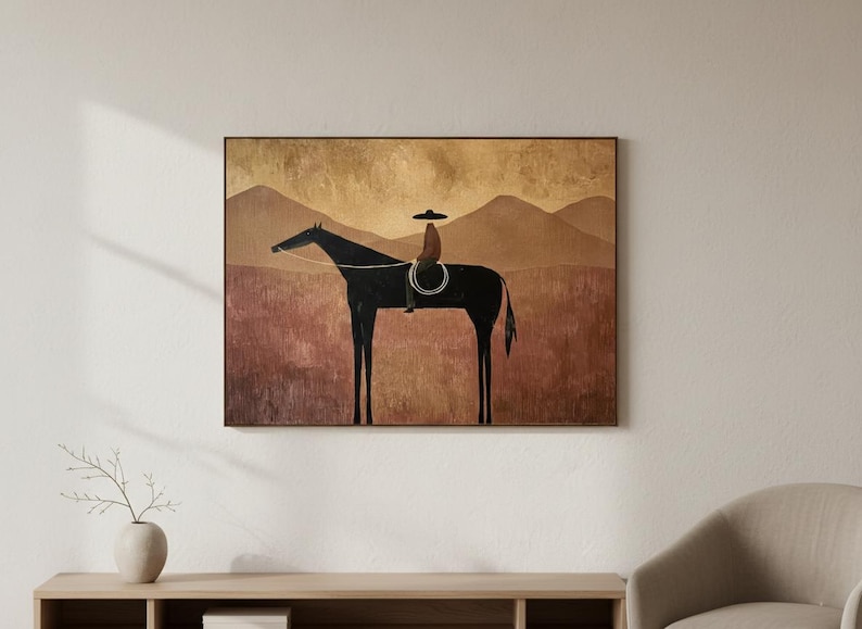 May include: A framed art print depicts a black horse with a rider wearing a hat, set against a backdrop of brown and gold mountains and a field. The artwork has a minimalist style and is mounted on a wooden frame.
