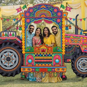 May include: A brightly painted tractor cutout with a detailed, colourful design. Four people are posing inside the cutout. The tractor is decorated with patterns and bright colours, set up outdoors, possibly for a celebration.