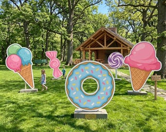 May include: Outdoor display featuring large, colorful cutouts of sweets. Includes an ice cream cone with pink, blue, and green scoops, a pink candy, a blue donut with sprinkles, a lollipop, and another ice cream cone. A wooden cabin is in the background.
