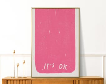 Può includere: Una stampa artistica incorniciata con un design rettangolare rosa e le parole "IT'S OK" in bianco. L'opera d'arte è esposta su un mobile in legno con candelabri dorati.