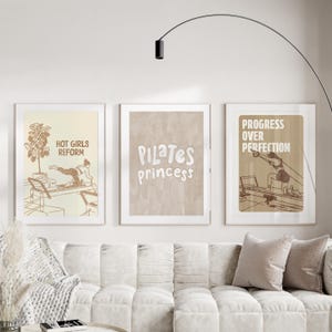 May include: Three framed art prints with a Pilates theme. The prints feature illustrations and text, including "Hot Girls Reform," "Pilates Princess," and "Progress Over Perfection." The color palette is neutral with beige and brown tones.