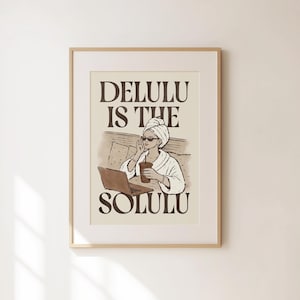 Puede incluir: Una lámina enmarcada con un dibujo lineal marrón de una persona con una toalla en la cabeza, gafas de sol y albornoz, sentada con un portátil y una bebida. El texto dice DELULU IS THE SOLULU en letras mayúsculas de color marrón.