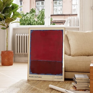 May include: A framed abstract painting by Mark Rothko, featuring a large red rectangle over a dark burgundy rectangle, with a thin blue border. The artwork is displayed in a living room setting, next to a beige sofa and a potted plant.