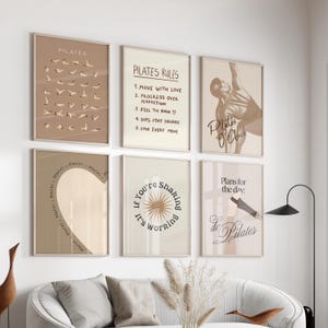 May include: A set of six framed Pilates-themed art prints in neutral tones. The prints feature Pilates poses, rules, and motivational phrases like "Pilates O'Clock" and "If you're shaking, it's working." The frames are a light brown color.