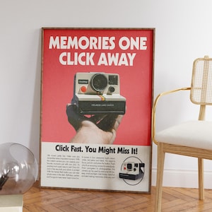 Op de afbeelding: Een ingelijste vintage Polaroid Land Camera-advertentie. De rode achtergrond bevat de tekst "MEMORIES ONE CLICK AWAY" en "Click Fast. You Might Miss It!". De camera wordt in een hand gehouden, met een kleine afbeelding van de camera.