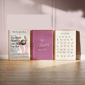 May include: Three framed posters with gold frames. The left poster is a newspaper-style print with the headline "Too Much Pilates Can Make You Hot." The center poster is a solid magenta color with the text "The Pilates Girl Club." The right poster displays Pilates poses.