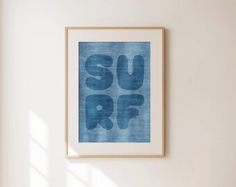 May include: Framed wall art featuring the word "SURF" in bold, blue letters against a textured blue background. The artwork is encased in a white mat and a light brown wooden frame, suitable for coastal or beach-themed decor.