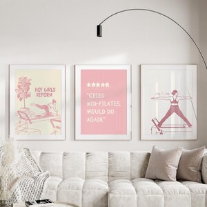 May include: Three framed art prints with pink and white designs. One print reads "HOT GIRLS REFORM" with a pilates reformer illustration. Another says "CRIED MID-PILATES, WOULD DO AGAIN." The third shows a person doing pilates.