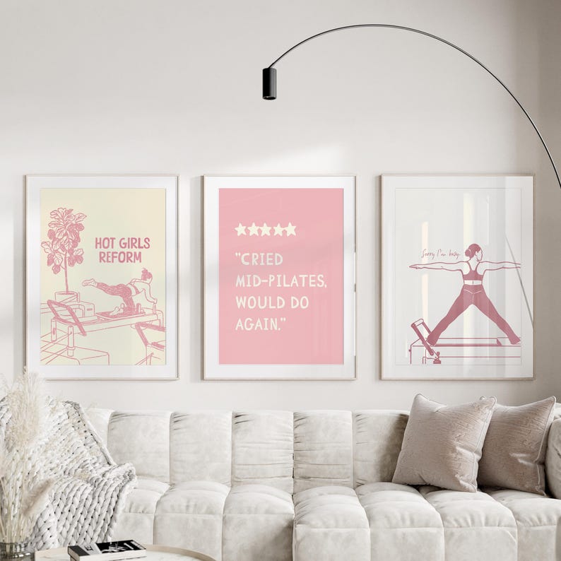 May include: Three framed art prints with pink and white designs. One print reads "HOT GIRLS REFORM" with a pilates reformer illustration. Another says "CRIED MID-PILATES, WOULD DO AGAIN." The third shows a person doing pilates.