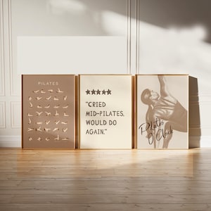 May include: Three framed Pilates-themed art prints. The left print is a taupe color with Pilates poses. The center print is cream-colored with the text "Cried Mid-Pilates, Would Do Again." The right print features a Pilates pose and the text "Pilates O'Clock."