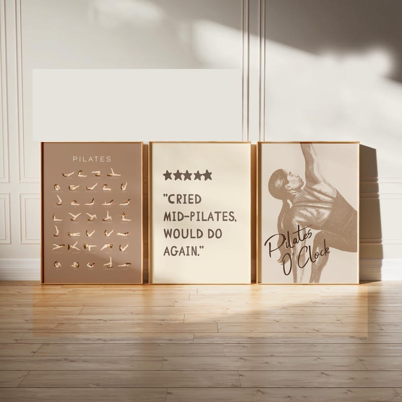 May include: Three framed Pilates-themed art prints. The left print is a taupe color with Pilates poses. The center print is cream-colored with the text "Cried Mid-Pilates, Would Do Again." The right print features a Pilates pose and the text "Pilates O'Clock."