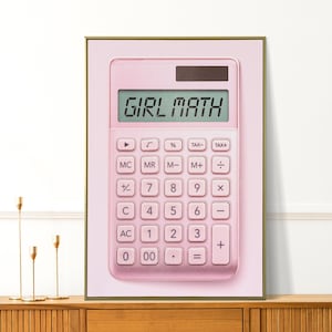 May include: A framed print showing a pink calculator with the text "GIRL MATH" on the display. The calculator has a standard button layout and is set against a soft pink background. The frame is gold.
