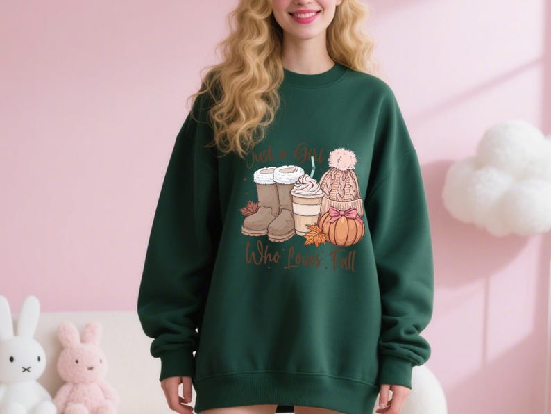 May include: Dark green sweatshirt with a fall-themed graphic. The graphic includes boots, a coffee drink, a hat, and a pumpkin. The text on the sweatshirt reads "Just a Girl Who Loves Fall."