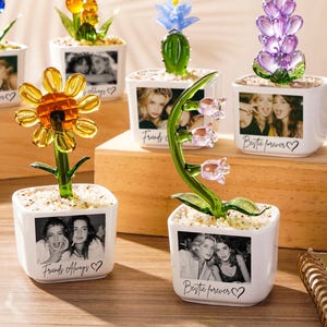 Peut inclure: Six pots de fleurs carrés en céramique blanche contenant des fleurs en verre de différentes couleurs. Chaque pot présente une photographie en noir et blanc sur le devant avec du texte comme "Bestie forever" ou "Friends Always" et un cœur.