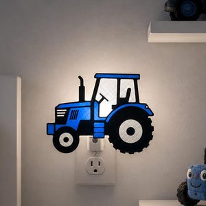 May include: A blue tractor night light plugged into a wall outlet. The night light is shaped like a tractor and has black wheels. A framed picture with the words "LITTLE FARMER" hangs on the wall. Other tractor-themed decorations are visible.