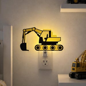 May include: A wall-mounted plug-in night light shaped like a yellow and black excavator. The light emits a soft glow from behind the silhouette of the construction vehicle, which is plugged directly into a standard wall socket on a light wall.