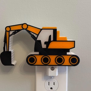 May include: A yellow, black, and white excavator-shaped night light plugged into a standard wall socket. The construction vehicle design features a prominent articulated arm, a bucket, and a tracked base, all rendered in a flat, layered style.