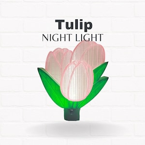 May include: A tulip-shaped night light with a pink flower and green leaves. The night light has the word "Tulip" above the words "NIGHT LIGHT". The night light is made of plastic and has a black base.