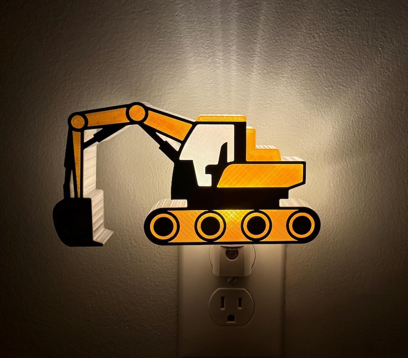 May include: A yellow and black excavator-shaped night light plugged into a wall socket. The construction vehicle design features a long articulated arm with a bucket, a cab, and tracked wheels, emitting a warm glow from behind the structure.