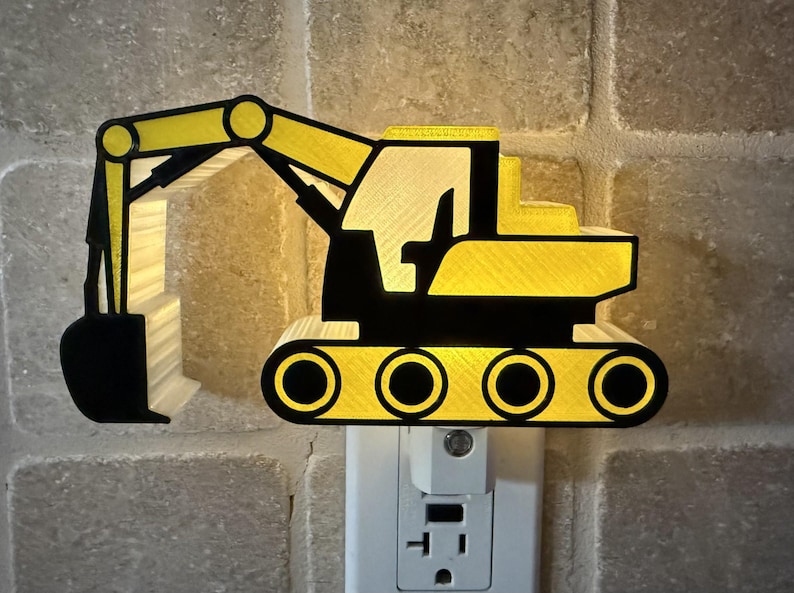 May include: A yellow and black excavator-shaped night light plugged into a wall socket. The construction vehicle design features a prominent bucket arm, a cab, and tracked wheels, emitting a soft glow from behind the structure to illuminate the area.