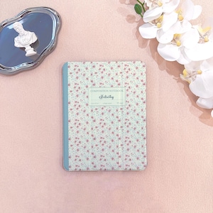 Peut inclure: Un cahier de composition floral avec le mot "Felicity" sur la couverture. Le cahier a une tranche bleu clair et un fond vert clair orné de petites fleurs roses. Les mots "Composition Notebook" sont en haut.