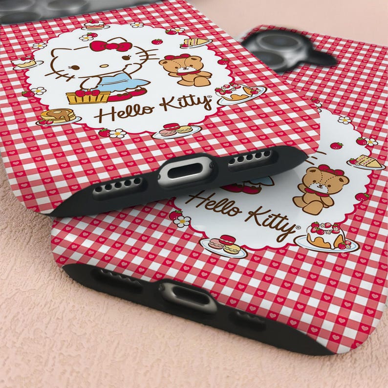 May include: Two black phone cases with a red and white gingham pattern. Each case features a white oval with Hello Kitty and a teddy bear illustration. The cases have cutouts for the camera and charging port.