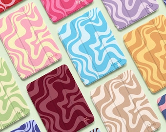Könnte beinhalten: Eine Sammlung rechteckiger Tablet-Hüllen mit einem wellenförmigen, marmorierten Muster in verschiedenen Farbkombinationen wie Rot, Pink, Blau, Lila, Gelb und Braun. Mehrere Hüllen sind mit Namen wie Elise, Emma und Lisa personalisiert.