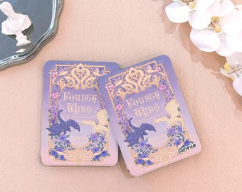 May include: Two rectangular, lavender-colored items with the text "Fourth Wing" and a dragon illustration. The items are decorated with floral and ornate scrollwork designs. The name "Annie" is printed on the bottom right corner.