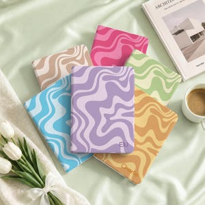 May include: A collection of six rectangular notebooks featuring wavy, marbled patterns in various colors including pink, purple, blue, tan, green, and orange. Two notebooks display personalized text, with one showing the letters EN and another the name Charlie.