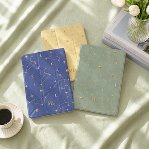 May include: Three rectangular tablet cases in blue, yellow, and sage green, each featuring gold foil constellations, stars, and crescent moons. The blue and green cases are personalized with the gold letters ML at the bottom center.