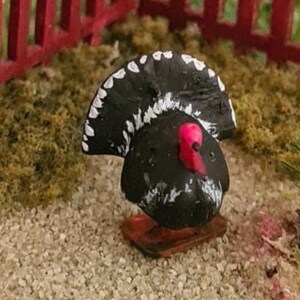 May include: Miniature black and white bird figurine with a red beak and head, standing on a small wooden base. The bird is in a miniature garden setting with a red picket fence and green grass.