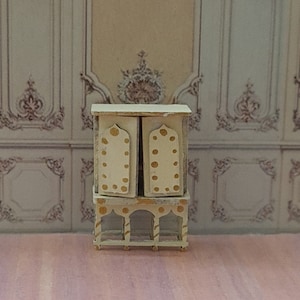 May include: A white miniature cabinet with gold accents and a decorative open base. The cabinet has two doors with gold polka dots and arched details.