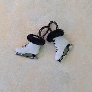 May include: Two miniature white ice skates with black faux fur trim and brown loops. The skates have silver blades and black laces. These decorative ornaments are perfect for winter holiday decor.