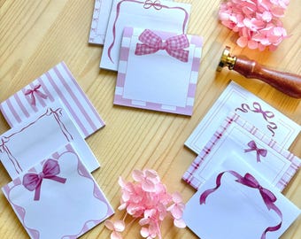 Peut inclure: Plusieurs blocs-notes roses et blancs avec des motifs de nœuds, disposés sur une surface en bois. Les blocs-notes présentent différents styles et motifs de nœuds, y compris des rayures et du vichy. Un tampon à cacheter en bois et des fleurs roses sont également présents.