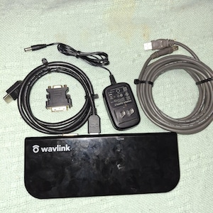 May include: A black Wavlink device with multiple cables and a power supply. Cables include HDMI, VGA, and USB. The power supply is black with a two-prong plug. The cables are black and gray.
