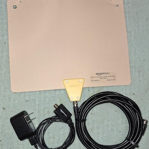 May include: An ultra-thin indoor HDTV antenna with a 50-mile range, amplifier, and power adapter. The antenna is beige, with a yellow triangular connector. The set includes a black power adapter and a black coaxial cable.