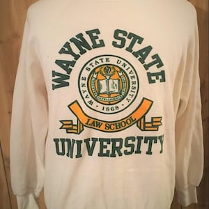 May include: Cream-colored Wayne State University Law School sweatshirt. The front features a circular emblem with the words "Wayne State University" and "1868." Below the emblem is the text "Law School University" in green and orange.