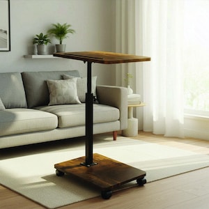 May include: A brown, height-adjustable laptop desk with a rectangular tabletop and base. The desk has a black metal support and sits on four small wheels. The tabletop and base have a wood grain finish. The desk is in a living room setting.