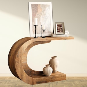 May include: A unique, curved wooden console table with a warm, natural finish. The table features a shelf with decorative items, including framed art, candles, and vases. The design is modern and sculptural, suitable for a living room or entryway.
