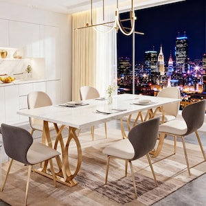 May include: A modern dining room set featuring a rectangular white marble-look table with a gold-colored base. Six upholstered chairs with gold legs surround the table. The room has a large window with a city skyline view.