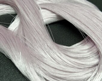 May include: Close-up of a bundle of pale lavender-colored thread. The thread is tightly spun and has a slight sheen, with individual strands visible. The threads are arranged in a loose, flowing pattern, suggesting a textile or craft material.